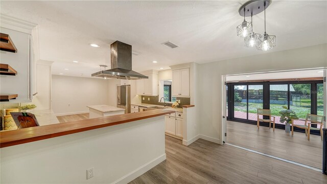 6990 Richardson Rd, Sarasota, FL 34240 - kitchen with island range hood, a sink, light wood-style floors, tasteful backsplash, and white cabinets