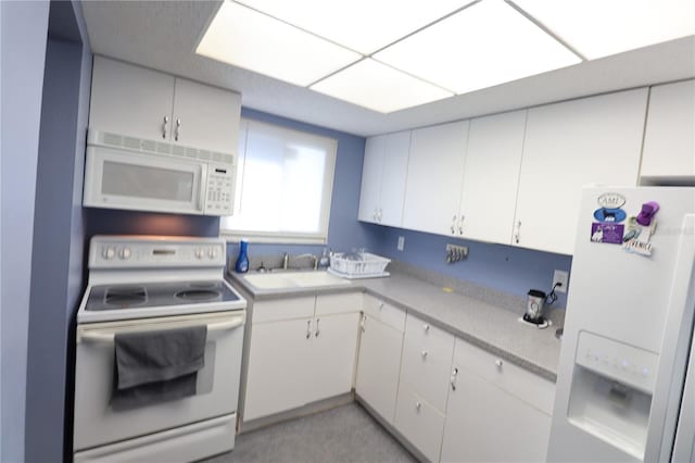 kitchen featuring white appliances, white cabinets, light countertops, and a sink