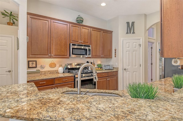 12358 Lavender Loop, Bradenton, FL 34212 - kitchen featuring appliances with stainless steel finishes, a sink, arched walkways, light stone counters, and brown cabinets