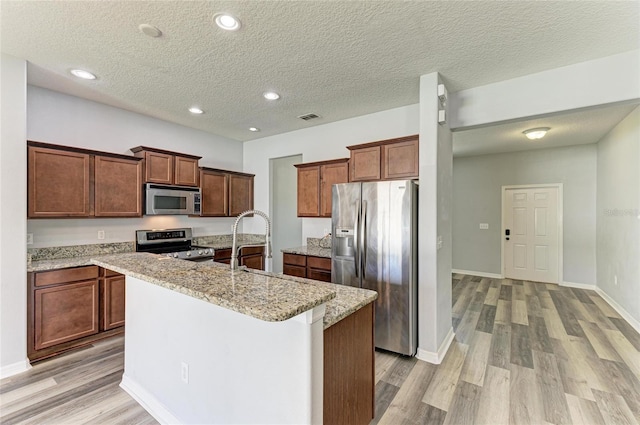 1721 Palm Warbler Ln, Ruskin, FL 33570 - kitchen featuring appliances with stainless steel finishes, light wood-style floors, an island with sink, recessed lighting, and light stone counters