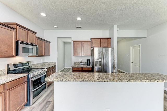 1721 Palm Warbler Ln, Ruskin, FL 33570 - kitchen featuring appliances with stainless steel finishes, light wood-style floors, a center island, light stone countertops, and a textured ceiling