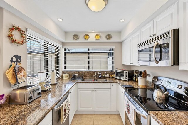 3914 Glen Oaks Manor Dr, Sarasota, FL 34232 - kitchen featuring stainless steel appliances, a sink, white cabinets, light tile patterned flooring, and dark stone countertops