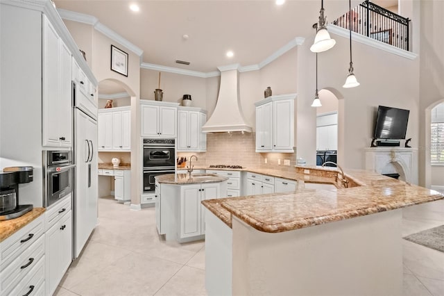 6808 Belmont Ct, Lakewood Ranch, FL 34202 - kitchen with custom range hood, light tile patterned floors, a kitchen island with sink, a sink, and crown molding