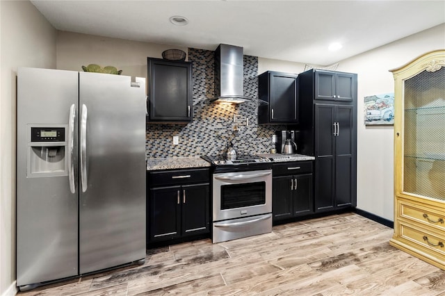 2306 63rd St W Unit 40, Bradenton, FL 34209 - kitchen with stainless steel appliances, wall chimney range hood, light wood-style flooring, dark cabinetry, and backsplash