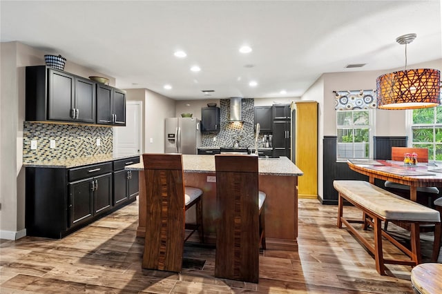 2306 63rd St W Unit 40, Bradenton, FL 34209 - kitchen with stainless steel fridge, wall chimney exhaust hood, a center island with sink, decorative backsplash, and light wood-style floors