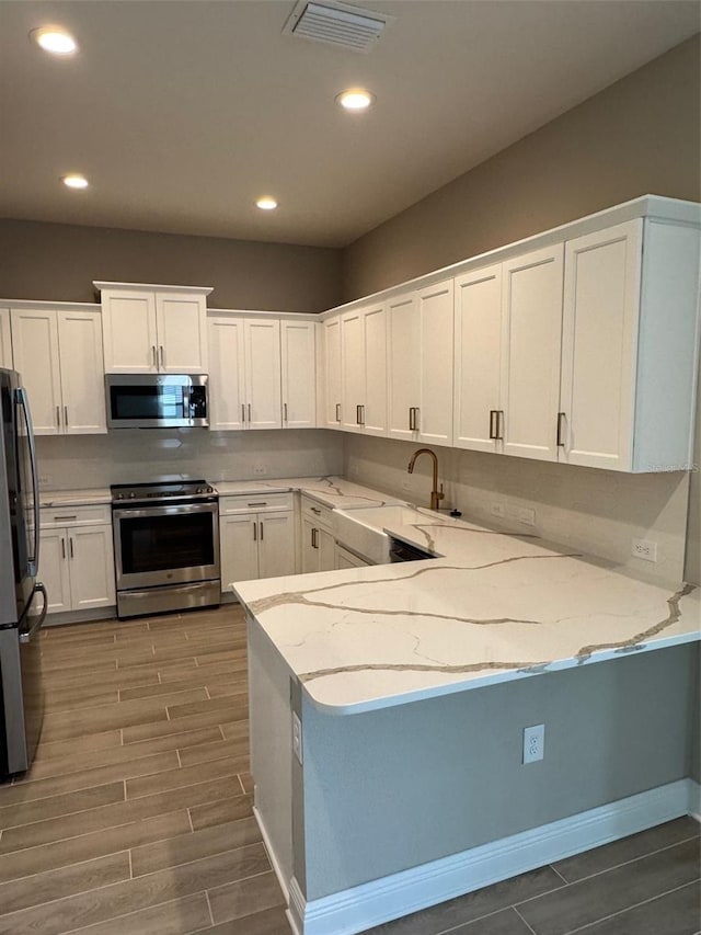 24831 Buckingham Way, Port Charlotte, FL 33980 - kitchen featuring stainless steel appliances, a peninsula, light stone countertops, white cabinets, and recessed lighting