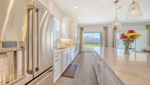 11427 Viani Ter, Palmetto, FL 34221 - kitchen featuring high end refrigerator, a sink, white cabinetry, hanging light fixtures, and light stone counters