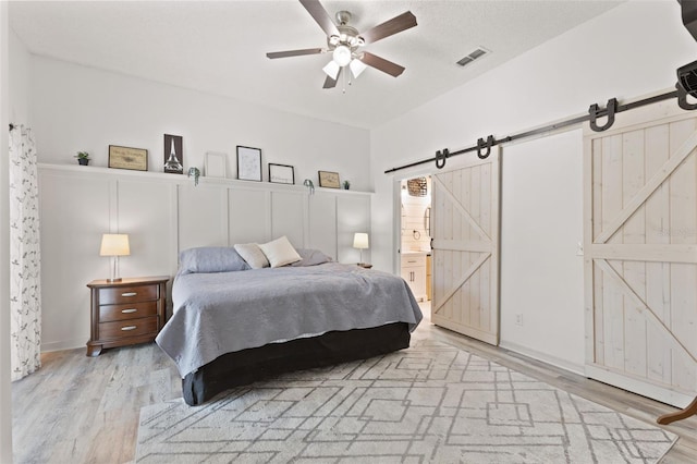 318 39th St NE, Bradenton, FL 34208 - bedroom with a barn door, light wood-style flooring, ensuite bathroom, and ceiling fan