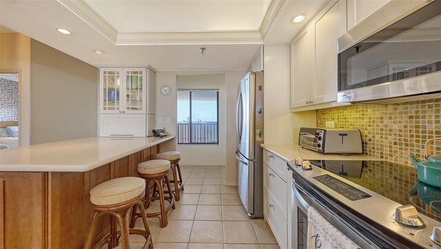 1465 Gulf Of Mexico Dr Unit 502, Longboat Key, FL 34228 - kitchen with stainless steel appliances, a kitchen breakfast bar, backsplash, white cabinets, and glass insert cabinets