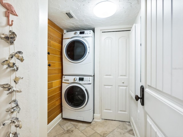 5880 Midnight Pass Rd Unit 207, Sarasota, FL 34242 - laundry area featuring stacked washing machine and dryer, light stone finish floors, wood walls, and baseboards