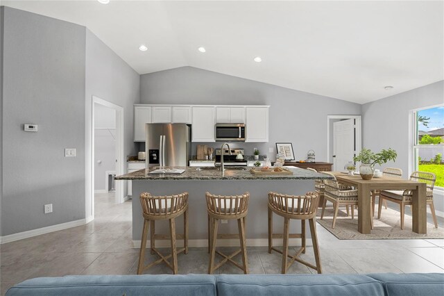 10547 Kidron Ave, Englewood, FL 34224 - kitchen featuring appliances with stainless steel finishes, a center island with sink, vaulted ceiling, a kitchen breakfast bar, and white cabinets