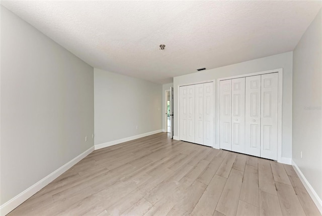 7023 Woodside Oaks Cir Unit 1, Sarasota, FL 34231 - unfurnished bedroom featuring two closets, light wood-style floors, baseboards, and a textured ceiling