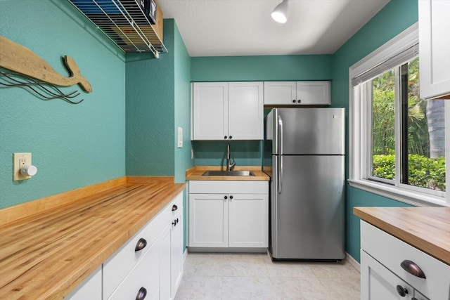 7321 Hemlock Ln, Sarasota, FL 34241 - kitchen featuring freestanding refrigerator, wood counters, a sink, white cabinetry, and light tile patterned floors