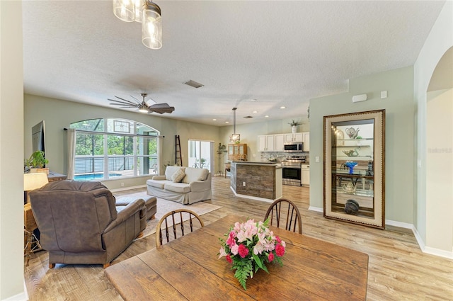 11254 82nd St E, Parrish, FL 34219 - dining space with a textured ceiling, light wood-style floors, baseboards, ceiling fan, and arched walkways