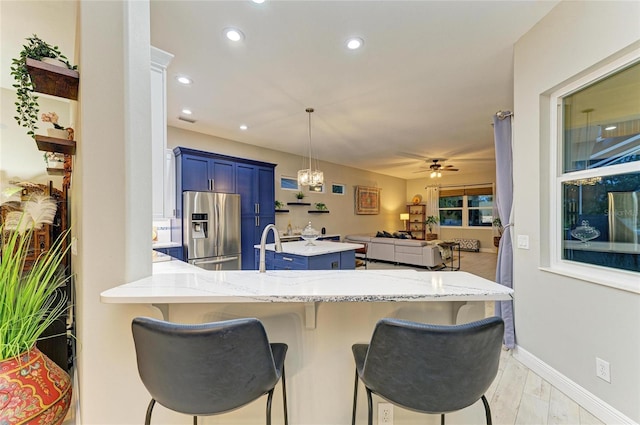 12175 Maple Ridge Dr, Parrish, FL 34219 - kitchen with stainless steel fridge, blue cabinets, a peninsula, light stone countertops, and a kitchen bar