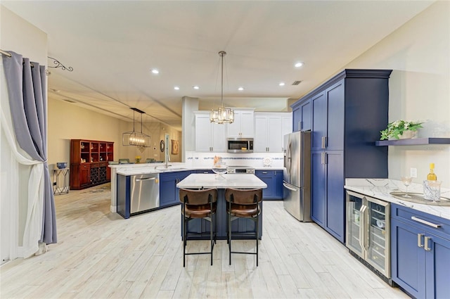 12175 Maple Ridge Dr, Parrish, FL 34219 - kitchen with stainless steel appliances, blue cabinetry, light wood-style flooring, a center island, and a chandelier