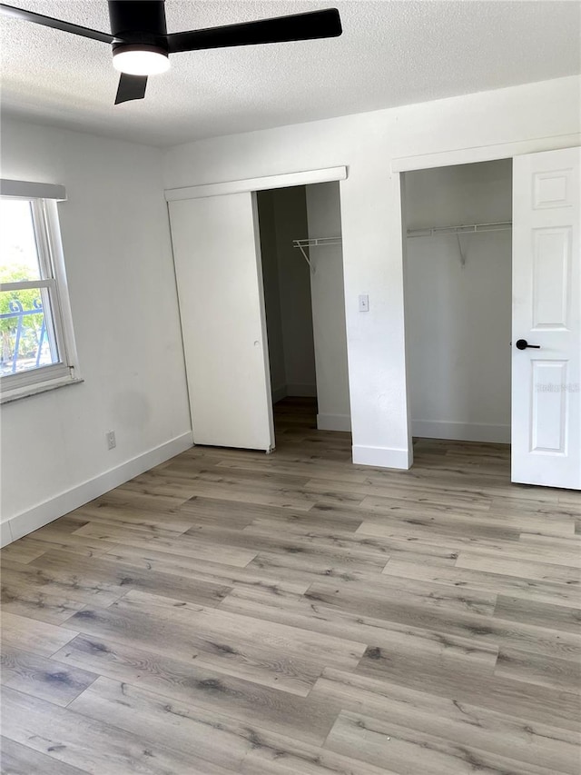 1947 Los Lomas Dr, Clearwater, FL 33763 - unfurnished bedroom featuring two closets, wood finished floors, baseboards, ceiling fan, and a textured ceiling