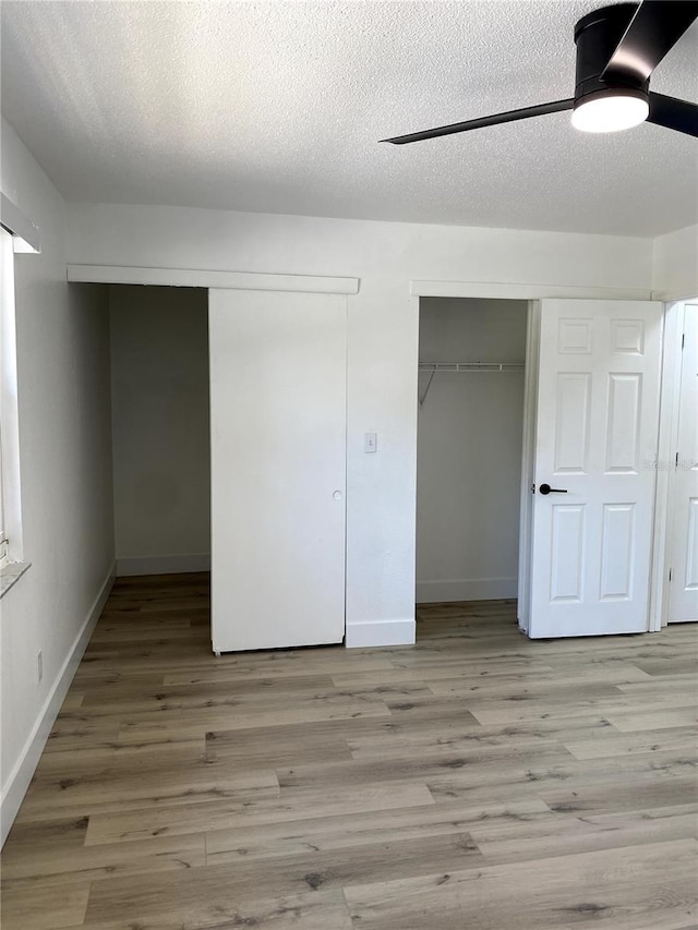 1947 Los Lomas Dr, Clearwater, FL 33763 - unfurnished bedroom featuring wood finished floors, baseboards, a ceiling fan, a textured ceiling, and two closets