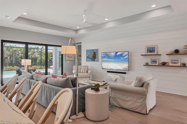 8020 Clearwater Ct, Sarasota, FL 34241 - living area featuring light wood finished floors, a tray ceiling, a ceiling fan, wood walls, and recessed lighting