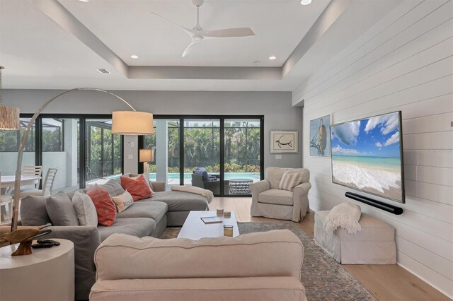8020 Clearwater Ct, Sarasota, FL 34241 - living room featuring wood finished floors, wooden walls, a tray ceiling, ceiling fan, and recessed lighting