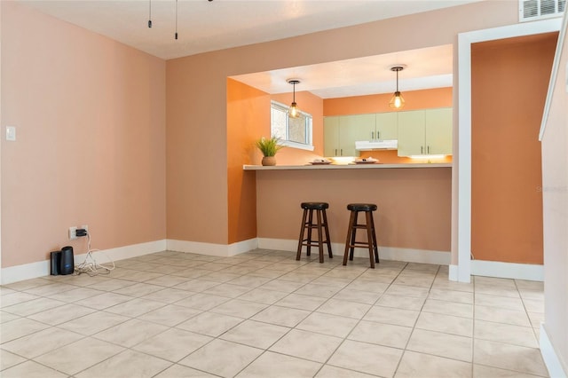 4475 Sandner Dr, Sarasota, FL 34243 - kitchen with under cabinet range hood, a kitchen breakfast bar, pendant lighting, light tile patterned floors, and baseboards