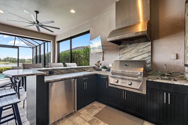 12856 Sorrento Way, Bradenton, FL 34211 - kitchen with refrigerator, wall chimney range hood, dark cabinetry, a ceiling fan, and a textured ceiling