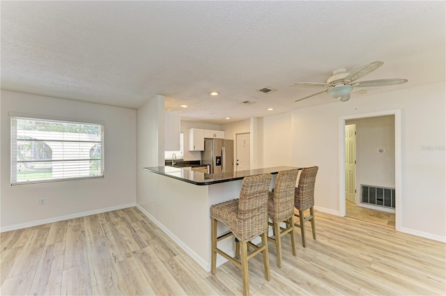 5223 Shadow Lawn Dr, Sarasota, FL 34242 - kitchen with stainless steel fridge, light wood-type flooring, white cabinets, dark countertops, and a textured ceiling
