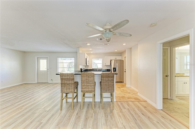 5223 Shadow Lawn Dr, Sarasota, FL 34242 - kitchen featuring stainless steel fridge, light wood-type flooring, white cabinetry, a kitchen bar, and ceiling fan