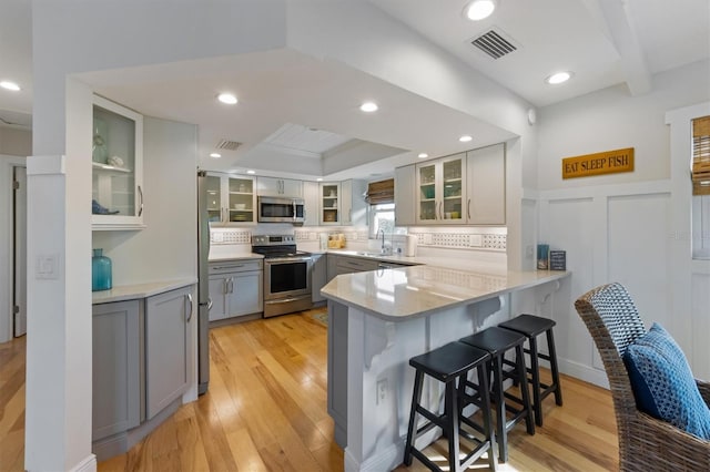221 85th St, Holmes Beach, FL 34217 - kitchen featuring appliances with stainless steel finishes, gray cabinetry, a peninsula, a breakfast bar area, and light wood-type flooring