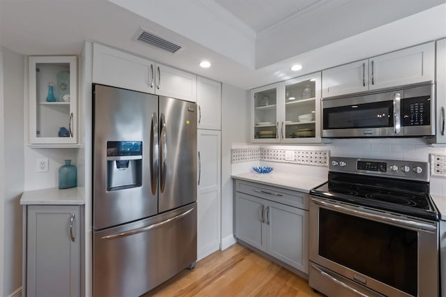221 85th St, Holmes Beach, FL 34217 - kitchen with stainless steel appliances, crown molding, decorative backsplash, light wood-type flooring, and glass insert cabinets