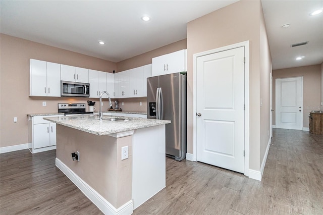 1229 Zinnia Loop, Labelle, FL 33935 - kitchen with appliances with stainless steel finishes, a sink, light wood-type flooring, a kitchen island with sink, and white cabinets