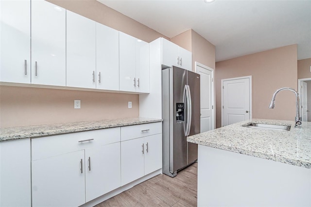 1229 Zinnia Loop, Labelle, FL 33935 - kitchen with stainless steel fridge, a sink, light wood-type flooring, white cabinets, and light stone counters