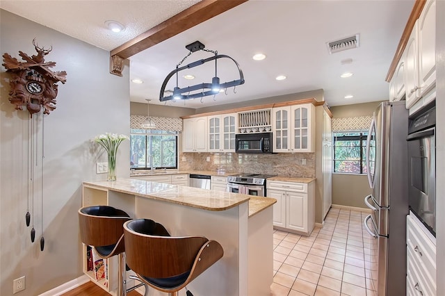 4917 Leatha Ln, Sarasota, FL 34232 - kitchen with appliances with stainless steel finishes, a peninsula, tasteful backsplash, glass insert cabinets, and healthy amount of natural light