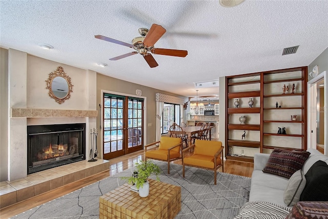 4917 Leatha Ln, Sarasota, FL 34232 - living room featuring wood finished floors, a ceiling fan, a textured ceiling, a tile fireplace, and french doors
