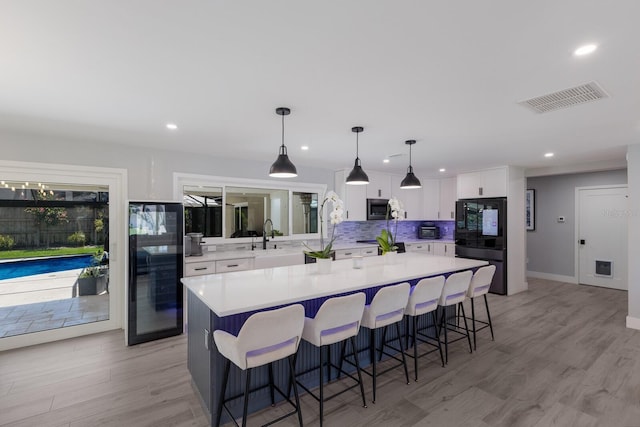 5581 Shadow Lawn Dr, Sarasota, FL 34242 - kitchen with stainless steel microwave, beverage cooler, white cabinetry, a breakfast bar area, and tasteful backsplash
