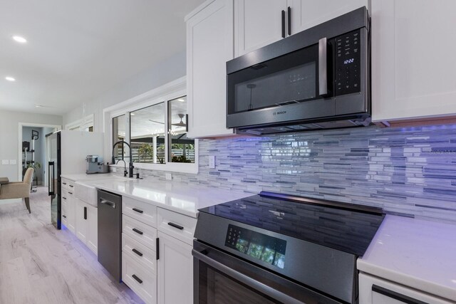 5581 Shadow Lawn Dr, Sarasota, FL 34242 - kitchen featuring stainless steel appliances, white cabinetry, backsplash, a sink, and light countertops