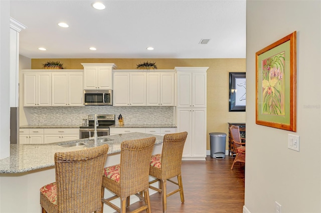 12229 Stuart Dr, Venice, FL 34293 - kitchen with stainless steel appliances, dark wood finished floors, a kitchen breakfast bar, backsplash, and white cabinets