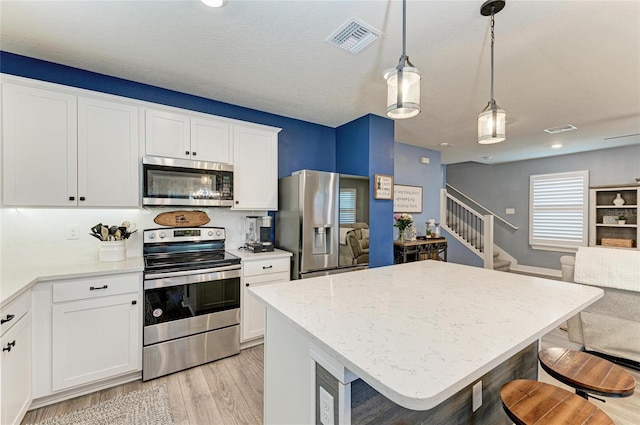 8940 Royal River Cir, Parrish, FL 34219 - kitchen with stainless steel appliances, light wood-type flooring, hanging light fixtures, open floor plan, and white cabinets