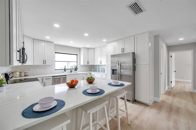 5125 Palm Aire Dr, Sarasota, FL 34243 - kitchen with stainless steel appliances, a peninsula, backsplash, light wood-type flooring, and light countertops