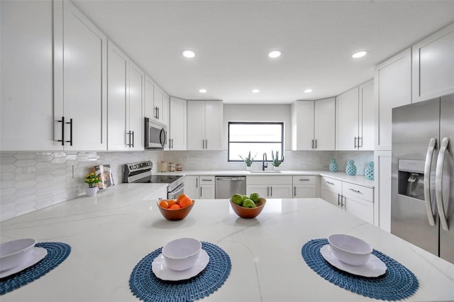 5125 Palm Aire Dr, Sarasota, FL 34243 - kitchen with stainless steel appliances, a sink, decorative backsplash, white cabinetry, and light stone counters