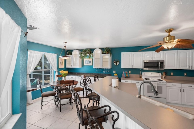 4222 Lanai Dr, Sarasota, FL 34241 - kitchen featuring white electric stove, stainless steel microwave, white cabinets, light tile patterned floors, and glass insert cabinets