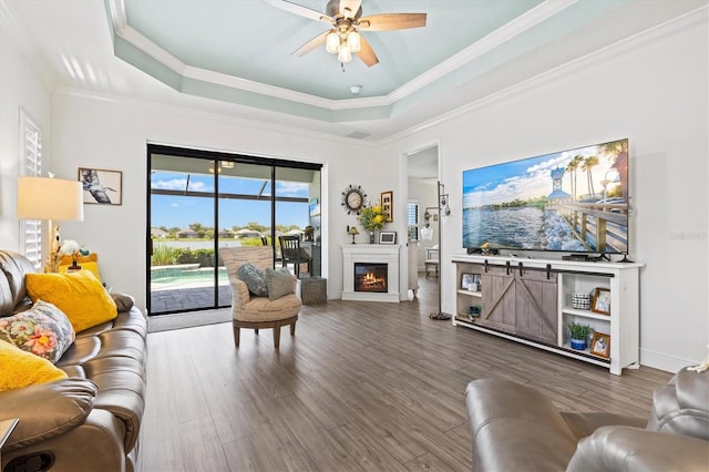 13849 Old Creek Ct, Parrish, FL 34219 - living room featuring a tray ceiling, wood finished floors, ceiling fan, crown molding, and a lit fireplace