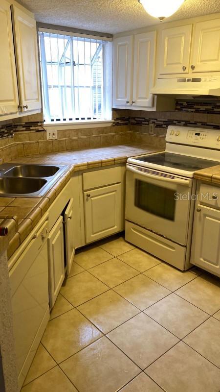 1948 Lake Atriums Cir Unit 132, Orlando, FL 32839 - kitchen with white electric range, under cabinet range hood, tile countertops, a textured ceiling, and light tile patterned flooring