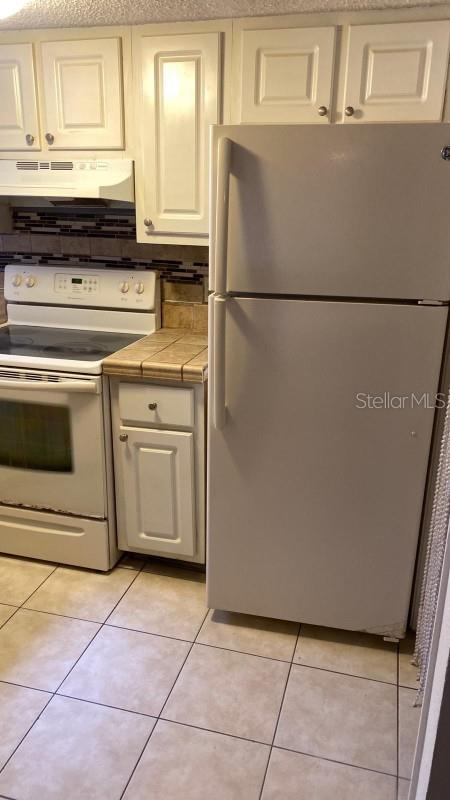 1948 Lake Atriums Cir Unit 132, Orlando, FL 32839 - kitchen featuring white appliances, tile countertops, under cabinet range hood, light tile patterned flooring, and white cabinets