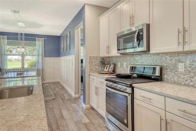 11502 Golden Bay Pl, Bradenton, FL 34211 - kitchen featuring appliances with stainless steel finishes, light wood-style floors, backsplash, white cabinetry, and a wainscoted wall