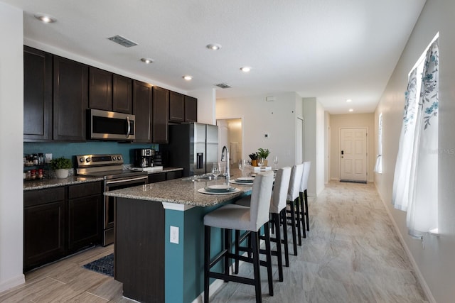 4739 Reisswood Loop, Palmetto, FL 34221 - kitchen featuring appliances with stainless steel finishes, a center island with sink, a kitchen bar, baseboards, and recessed lighting