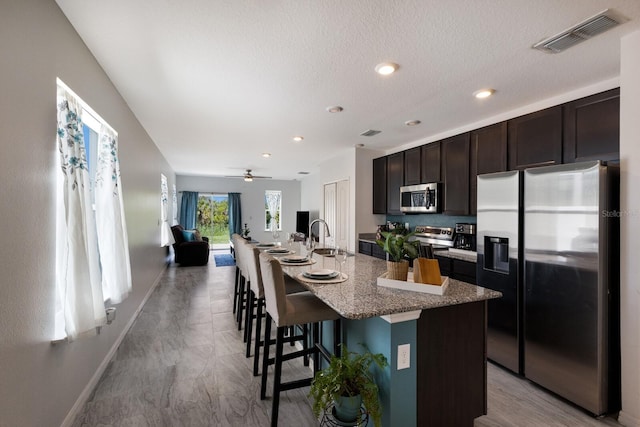4739 Reisswood Loop, Palmetto, FL 34221 - kitchen with stainless steel appliances, an island with sink, open floor plan, a sink, and dark brown cabinetry