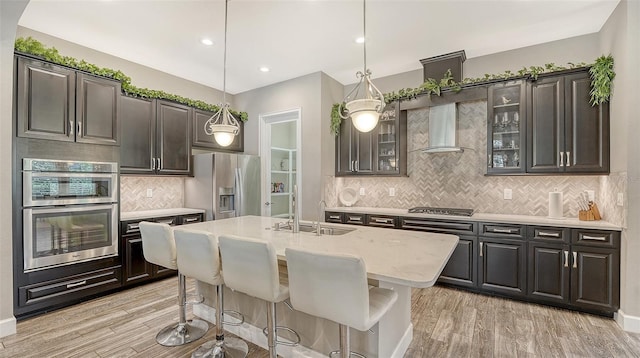 11603 Bluebird Pl, Lakewood Ranch, FL 34211 - kitchen featuring stainless steel appliances, a sink, wall chimney range hood, tasteful backsplash, and light wood finished floors