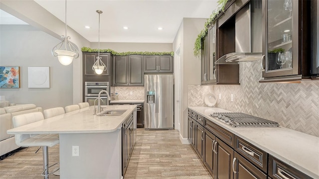 11603 Bluebird Pl, Lakewood Ranch, FL 34211 - kitchen featuring stainless steel appliances, wall chimney exhaust hood, a sink, a kitchen breakfast bar, and light wood-type flooring