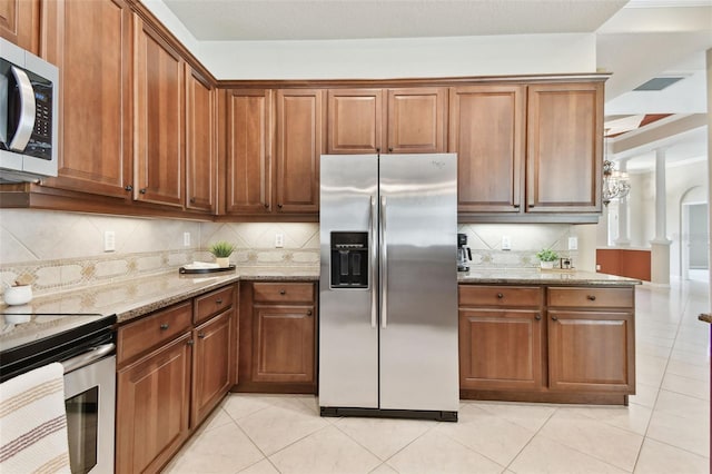 9008 Brookfield Ter, Bradenton, FL 34212 - kitchen with stainless steel appliances, light stone counters, light tile patterned floors, decorative backsplash, and brown cabinets
